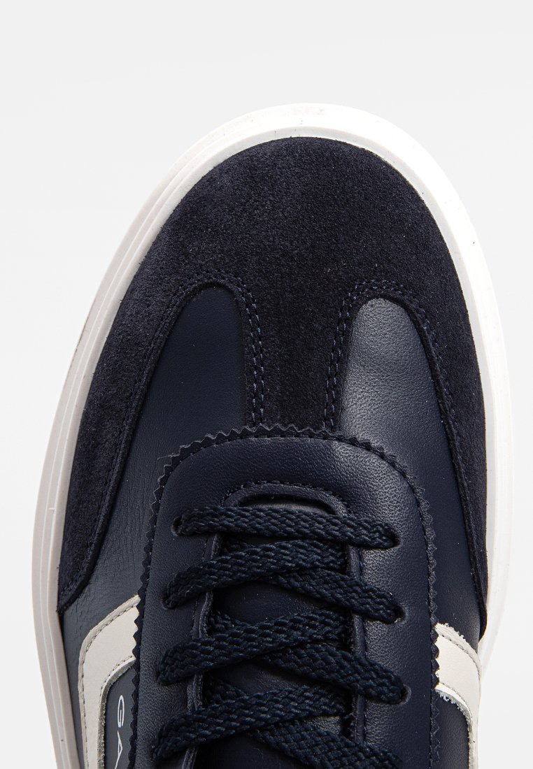 Marineblaue Sneaker mit Wildleder- und Ledertexturen, weißer Sohle und marineblauen geflochtenen Schnürsenkeln in einer Nahaufnahme von oben.