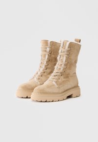 Bottes chevilles en daim beige avec un bout rond, un devant à lacets et une semelle en caoutchouc robuste. Caractéristiques : doublure douce et tirant à l'arrière.