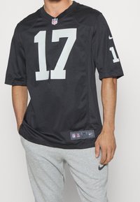 Mand i sort NFL-trøje med nummer 17 og grå Nike sweatpants, står med den ene hånd i lommen mod en hvid baggrund.