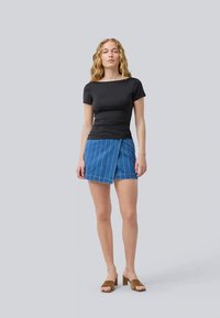 Top preto de manga curta combinado com uma saia envolvente de ganga azul com riscas brancas verticais. A modelo usa sandálias de salto castanhas.