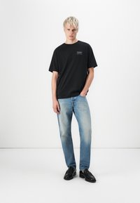 Sort bomulds t-shirt med rund hals, parret med lyseblå slidte jeans og sorte lædersko. Enkel design, afslappet pasform.