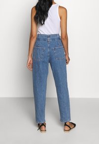 Korkeavyötäröiset siniset farkut rentoa leikkausta, joissa on kaksi takataskua, näkyvä ommel ja vyölenkki.