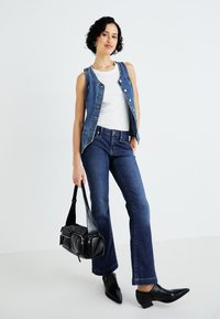Gilet in denim con bottoni frontali, top bianco, jeans blu a zampa d'elefante, borsa nera e stivaletti a punta. Texture lisce, schema di colori scuri.