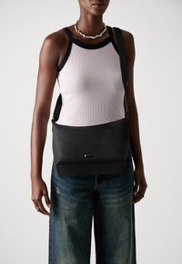Borsa a spalla nera realizzata in pelle liscia; presenta una forma rettangolare elegante e un'etichetta del marchio discreta; abbinata a una canotta a costine rosa chiaro.