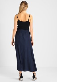 Černý top na tenkých ramínkách v kombinaci s dlouhou, splývavou sukní navy modré barvy. Sukně má elastický pas a hladký povrch.