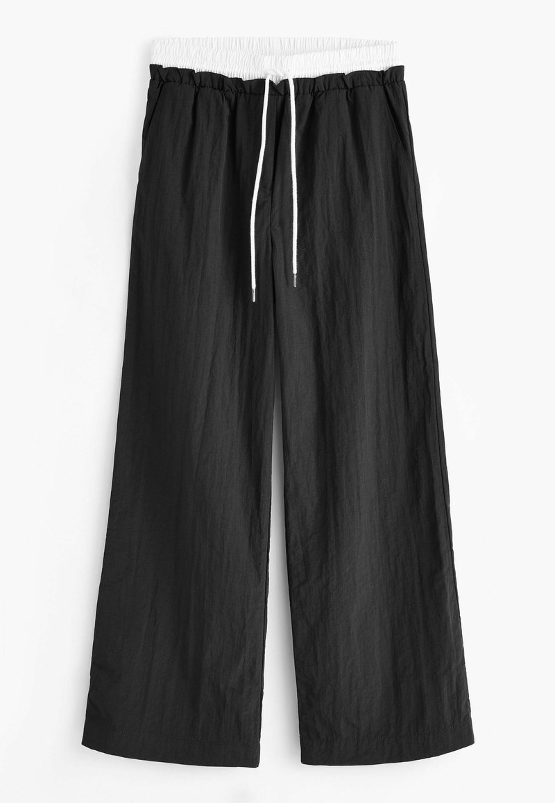 Pantalons larges noirs en tissu léger, dotés d'une ceinture élastique blanche avec cordon de serrage et d'une coupe décontractée.