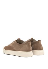 Braune Wildledersneaker mit einer weißen Gummisohle, runder Zehenform, Schnürdesign und einem kleinen mehrfarbigen Tab auf der Rückseite.