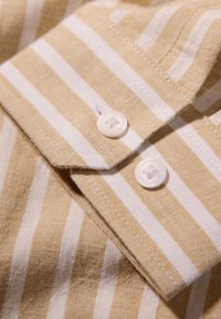 Lichtgele en witte gestreepte overhemd met knoopsluiting en een kraag, voorzien van twee ronde knopen nabij de kraag en een linnen textuur.