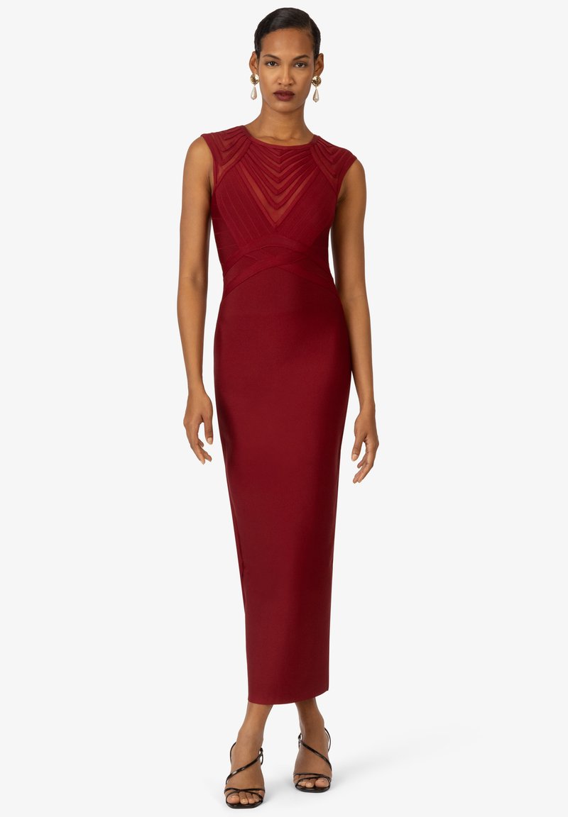 Rotes, eng anliegendes Kleid mit strukturiertem Oberteil, transparenter Detailgestaltung am Halsausschnitt und gerader Silhouette, die bis zur Mitte der Wade reicht. Kombinieren Sie es mit schwarzen Riemchenschuhen.