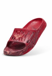 Sandale rouge à enfiler avec des fentes de ventilation, une semelle texturée et un logo ailé numéro un sur la bride, montrée sur fond blanc.