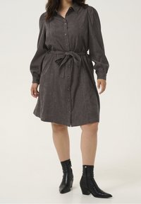 Grijze button-up jurk met lange pofmouwen en een strikceintuur, gemaakt van gestructureerde stof; gecombineerd met zwarte enkellaarsjes met een spitse neus.