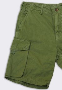 Pantaloni cargo verdi realizzati in un tessuto leggero con finitura testurizzata. Presentano tasche laterali e una chiusura con un solo bottone in vita.