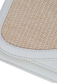 Gewebtes beiges Material mit einer strukturierten Oberfläche, umrahmt von glattem weißen Lederbesatz, mit präzisen Nähten und einer weichen, abgerundeten Form.