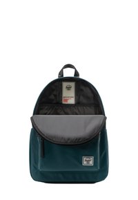Tarnfarbener Rucksack aus strapazierfähigem Stoff. Runde Oberseite, graue Klappe und eine Fronttasche. Das Innere hat ein Etikett und eine schwarze Innenauskleidung.