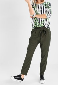 Top stampato con strisce verdi e nere e motivo foglioso; pantaloni a sigaretta verde oliva con nodo frontale; sneakers nere.