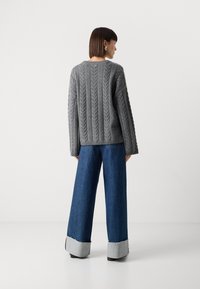 Pull en tricot gris avec un motif en maille torsadée, associé à un jean en denim foncé à jambes larges avec des poignets gris et des bords effilochés.