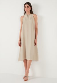 Beige halter dress with a relaxed fit, knee-length, made of lightweight fabric with a subtle texture. Features a gathered neckline.
