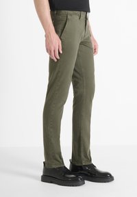 Pantalones en verde oliva, ajustados, fabricados con un tejido duradero, que presentan un diseño clásico de cinco bolsillos y un cierre de cremallera, combinados con zapatos negros.