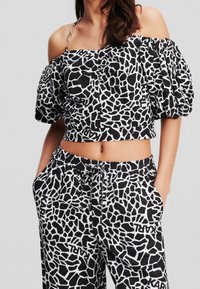 Zwart-witte crop top met puffy mouwen, voorzien van een geometrisch patroon. Gecombineerd met bijpassende broek met elastische taille, ook in hetzelfde patroon.