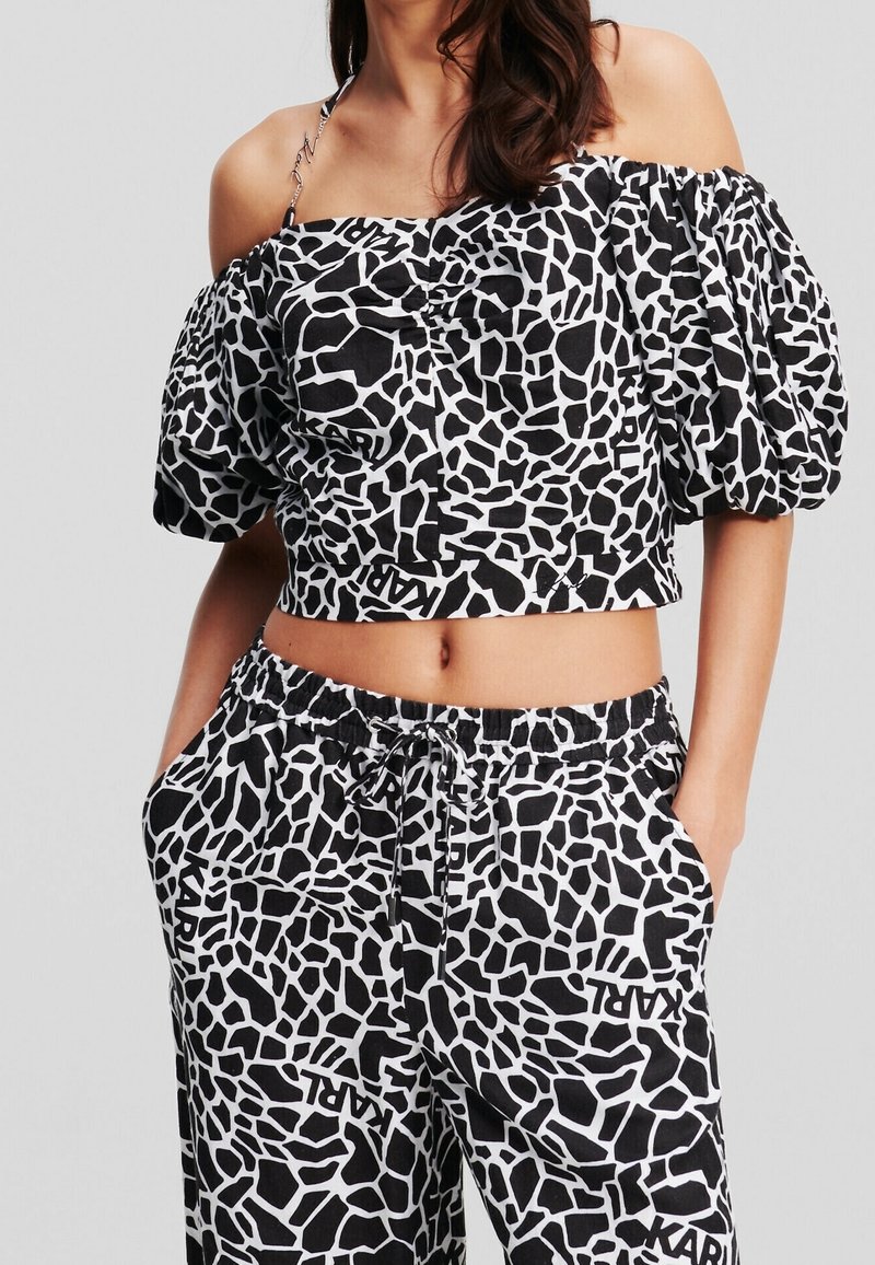 Zwart-witte crop top met puffy mouwen, voorzien van een geometrisch patroon. Gecombineerd met bijpassende broek met elastische taille, ook in hetzelfde patroon.