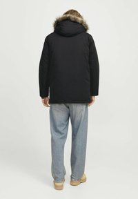 Sort parka-jakke med hætte trimmet med pels, med quiltet tekstur og afslappet pasform, parret med løse blå jeans og brune støvler.