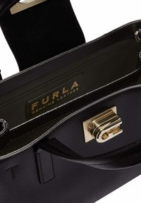 Sac à main en cuir véritable noir avec fermoir doré, texture lisse et poche intérieure zippée avec une étiquette portant le logo FURLA.