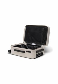 Valise rigide de couleur beige clair, avec un intérieur noir. Comprend un compartiment à fermeture éclair et des roues pour la mobilité. Ouverte, montrant le design intérieur.