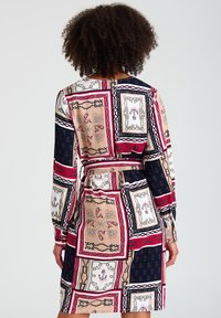 Langärmeliges Kleid mit einem mehrfarbigen Patchwork-Design aus Rahmen, Ketten und Blumenmustern in Rot-, Marine-, Creme- und Goldtönen.