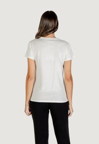 Camiseta de algodón blanca con mangas cortas, escote redondeado y un corte holgado, combinada con pantalones negros. La vista posterior enfatiza la simplicidad y la comodidad.