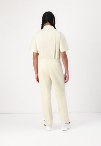 Ανοιχτό κίτρινα σορτς και αντίστοιχα παντελόνια με ελαστική ζώνη, σχεδιασμένα σαν πουκάμισο με γιακά, φαίνονται από πίσω, με λευκά αθλητικά παπούτσια.