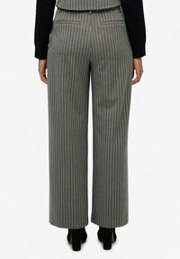 Szatkowane, szare spodnie o szerokich nogawkach z wysokim stanem, dwoma tylnymi kieszeniami i gładką fakturą. Noszone z czarnymi szpilkami.