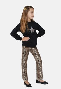 Černá mikina se třpytivým potiskem hvězdy, spárovaná s kalhotami s leopardím potiskem a černými baletkami. Dívka zaujímá profilový postoj.