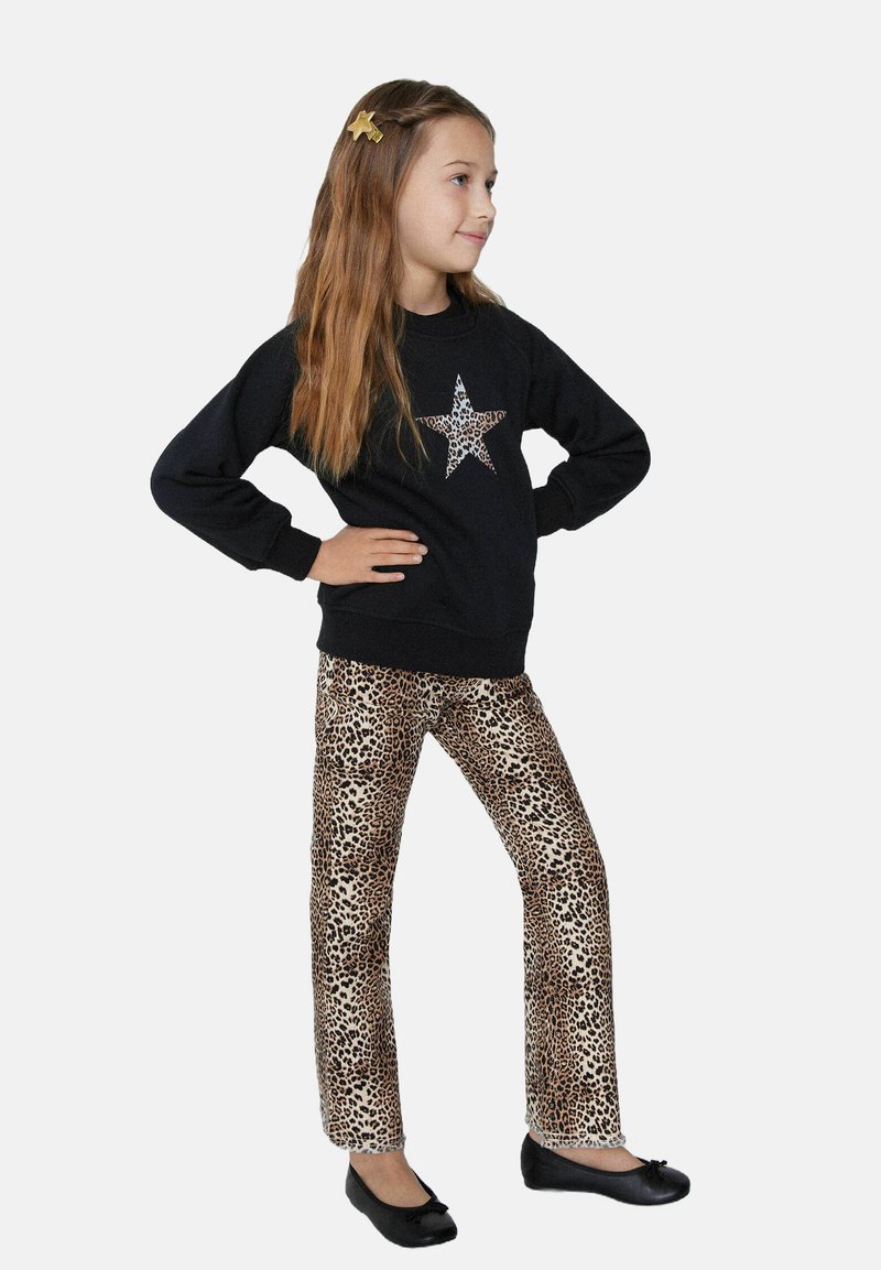 Černá mikina se třpytivým potiskem hvězdy, spárovaná s kalhotami s leopardím potiskem a černými baletkami. Dívka zaujímá profilový postoj.