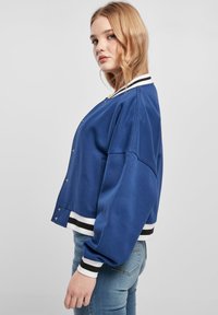 Blue cropped sweatshirt with white and black striped cuffs and hem, featuring snap-button closure and a loose fit design.