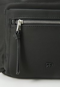 Fekete nylon táska, elülső cipzáras zsebbel, fém cipzárhúzóval és egy diszkrét logóval a jobb alsó sarokban.