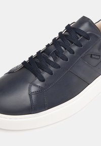 Sneakers in pelle blu navy con finitura liscia, dotati di lacci rotondi, suola in gomma bianca e un branding discreto sul lato.
