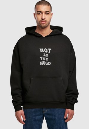 Sort hoodie med forlommer, prydet med hvid tekst "IKKE I HUMØR" i en stiliseret skrifttype. Fremstillet af blødt stof med en afslappet pasform.