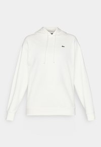 Hvit hettegenser laget av myk stoff, med lange ermer, justerbar hette, og en liten grønn logo på brystet.