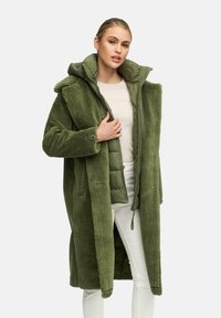 Groene, fuzzy buitenlaag met capuchon, met een rits binnenlaag in bijpassend groen. Lange mouwen en details van een sluiting aan de voorkant zijn zichtbaar.