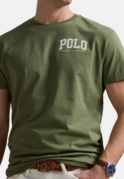 Camiseta de algodón verde oliva con el texto "POLO RALPH LAUREN" en blanco. Cuello redondo, mangas cortas, textura suave, combinada con un cinturón trenzado marrón.