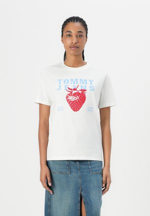 T-shirt en coton blanc avec un grand graphisme de fraise rouge et un texte bleu indiquant "TOMMY JEANS EST. 1988 N.Y.C. U.S.A." Manches courtes.