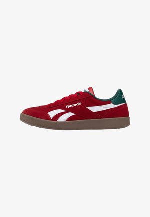 Sneaker rossa Reebok con strisce del logo bianche, colletto del tallone verde scuro, suola marrone e lacci rossi mostrata di profilo laterale.