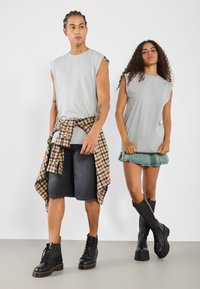 Sive majice brez rokavov, temni denim kratki hlač, in karirana srajca zavezana okoli pasu; v kombinaciji s črnimi platform škornji in denim mini krilom.