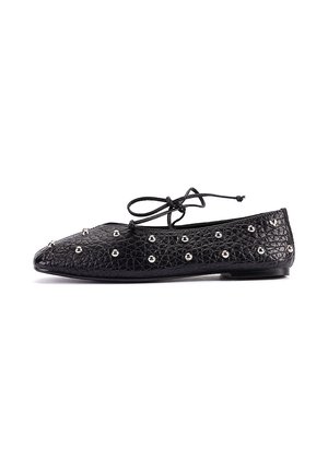 Zapato plano negro con superficie texturizada, tachuelas plateadas y detalle de cordones en la parte superior, mostrado de lado sobre un fondo blanco.