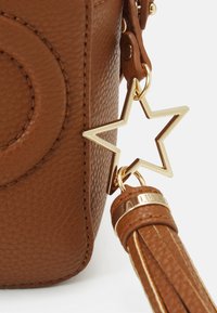 Borsa in pelle marrone con texture, caratterizzata da un charm a forma di stella dorata e un accento con frangia dotato di una banda metallica. Pattern circolare impressa sulla superficie.