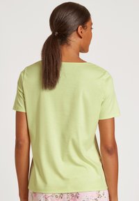 Korte mouw, ronde hals T-shirt van lichtgroene katoen, met een gladde textuur en een relaxed fit. Zichtbaar haar in een paardenstaart, met bloemen pyjamabroeken.
