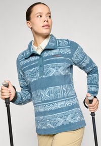 Blå fleecepullover med hvide geometriske mønstre, halvlys foran og krave. Har et logo-patch og sidelommer. Ideel til udendørs brug.