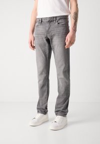 Jeans de mezclilla gris con un corte ajustado, diseño de cinco bolsillos y un ligero desvanecimiento. Cuenta con cierre de botón y cremallera metálicos, combinados con zapatillas blancas.
