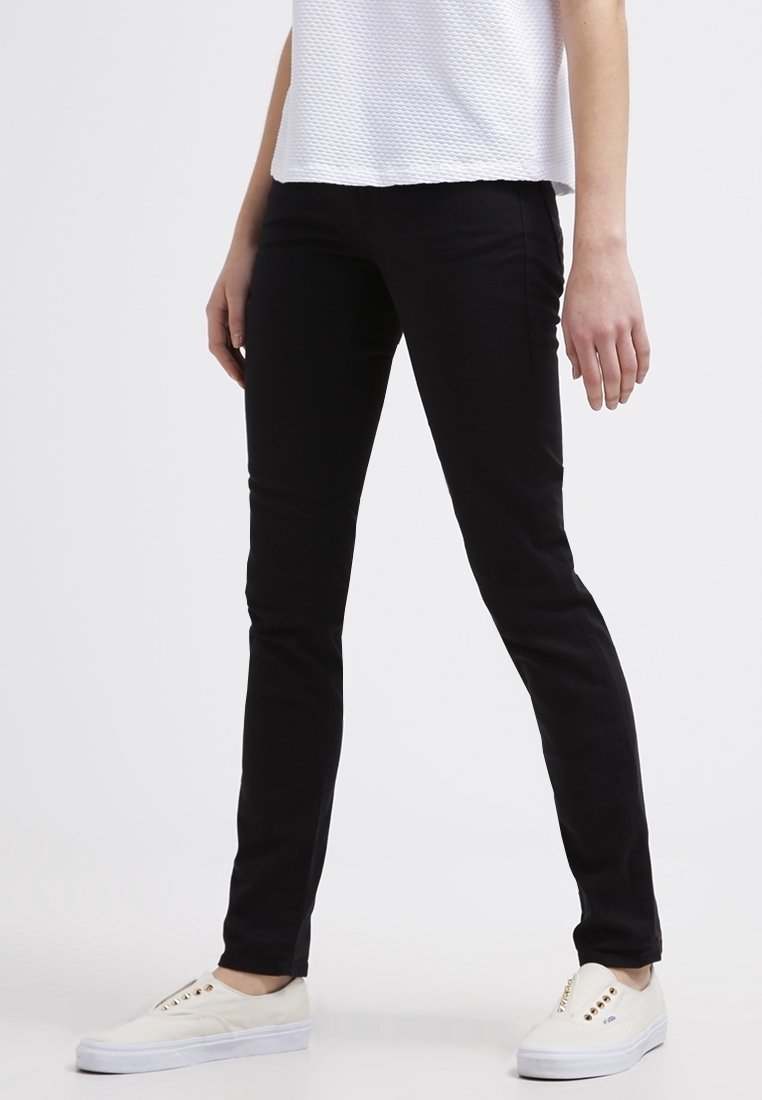 Pantalones ajustados negros de mezcla de algodón; textura suave, cintura mediana y diseño de cinco bolsillos. Combinados con zapatillas blancas sin cordones.