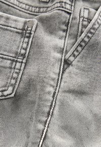 Close-up of gray denim jeans showing front pocket, metal rivet, and double-stitched seams with visible fabric texture.